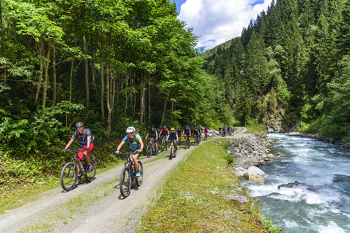 eine Gruppe Mountainbiker fhrt an einem Wildbach in den Alpen en