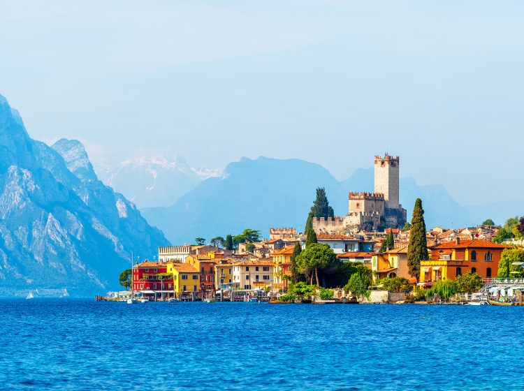 Ancient tower and fortress in old town Malcesine at Garda lake, Veneto region, Italy. High snowbound top mountains on background. Summer landscape with colorful houses and green trees.