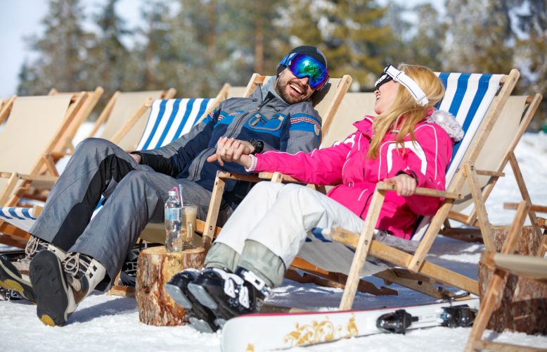 Cheerful man and woman in love sunbathing in sun lounger on skiing